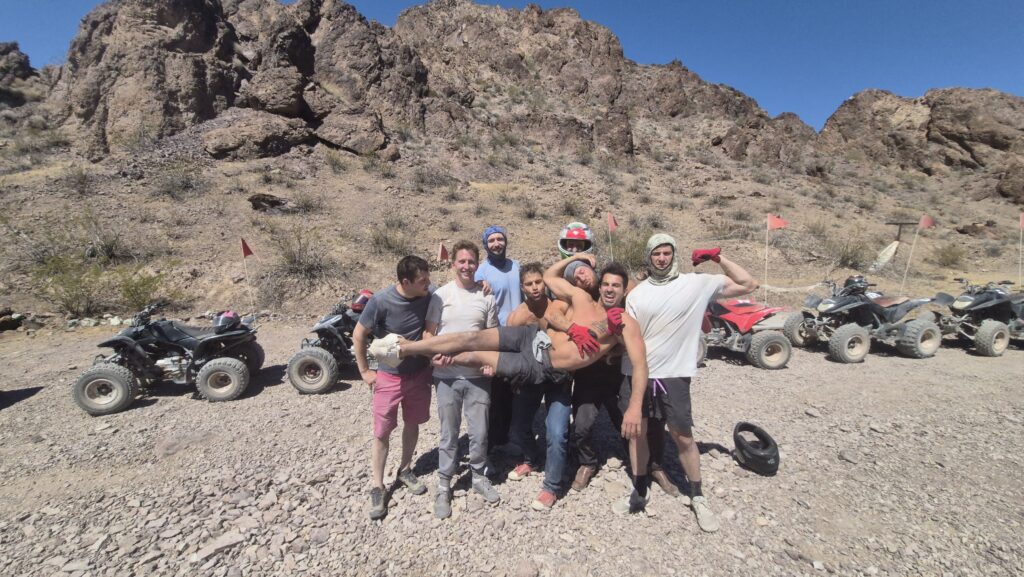 Group of seven men pose in Nevada desert near Las Vegas with ATVs after an exciting RZR off-road tour under a clear blue sky.