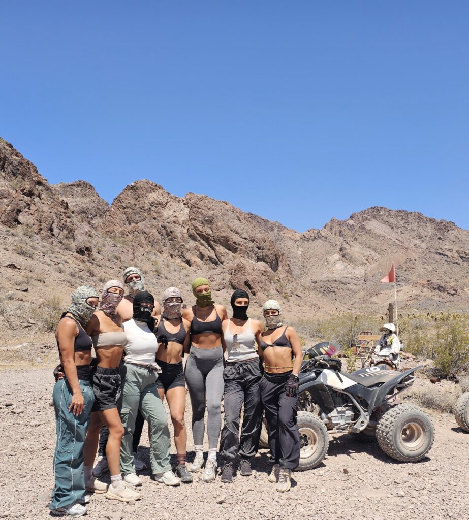 Women in activewear pose on a Nevada desert trail near an ATV, mountains behind; Las Vegas RZR off-road adventure.
