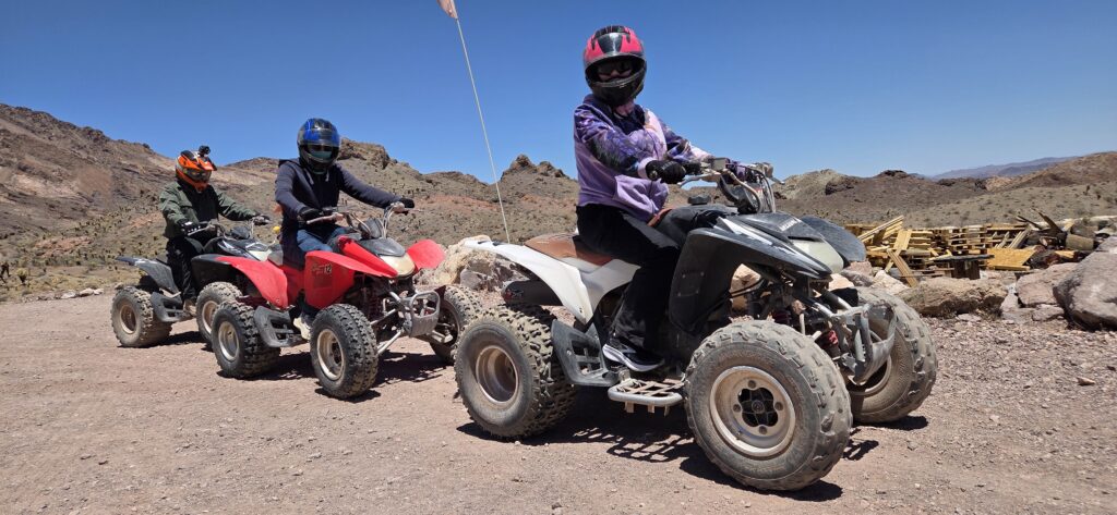 Adventurers in helmets ride ATVs on a rocky Nevada desert trail near mountains under clear skies during a Las Vegas ATV tour.