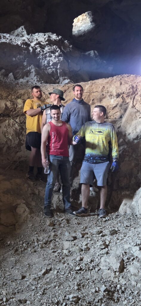 Group of men exploring a rocky Nevada cave near the Colorado River, smiling during their Las Vegas ATV tour adventure.
