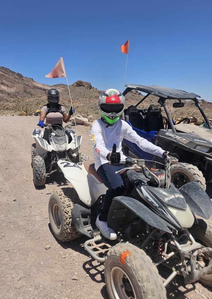 ATV riders in helmets explore a rocky Nevada desert near Las Vegas with RZR off-road tours and orange flags under clear skies.