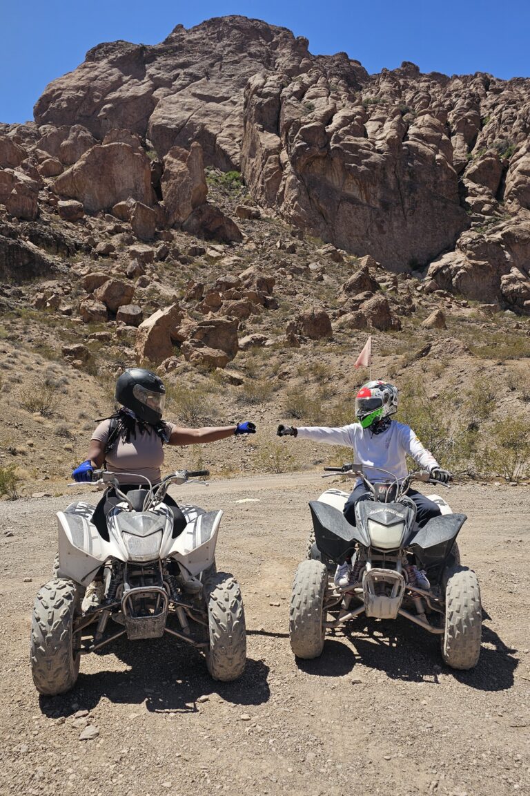 Riders on ATVs in Nevada's rocky desert near Las Vegas fist bump during an exciting ATV tour under a clear blue sky.