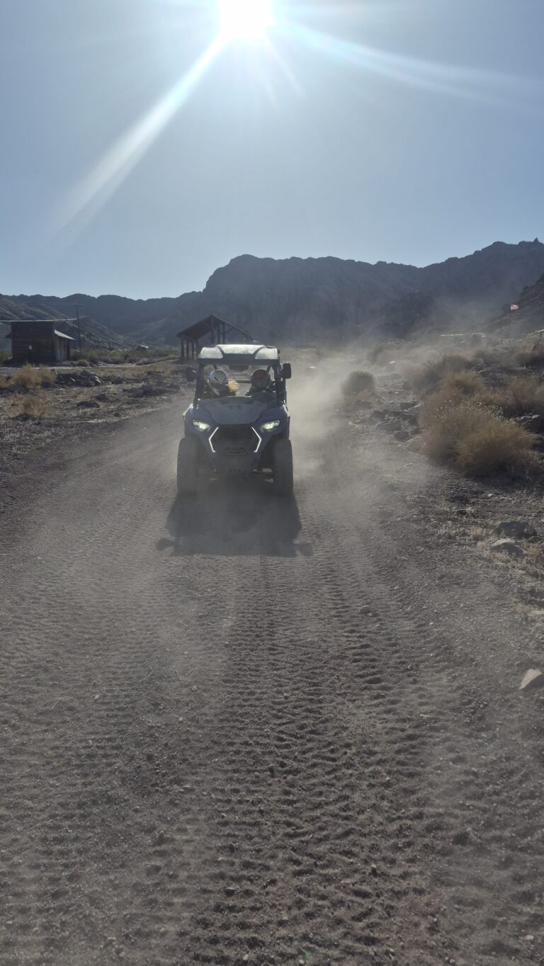 Experience an RZR off-road ride near Las Vegas, Nevada, on a dusty trail with mountains and sparse desert scenery in the background.