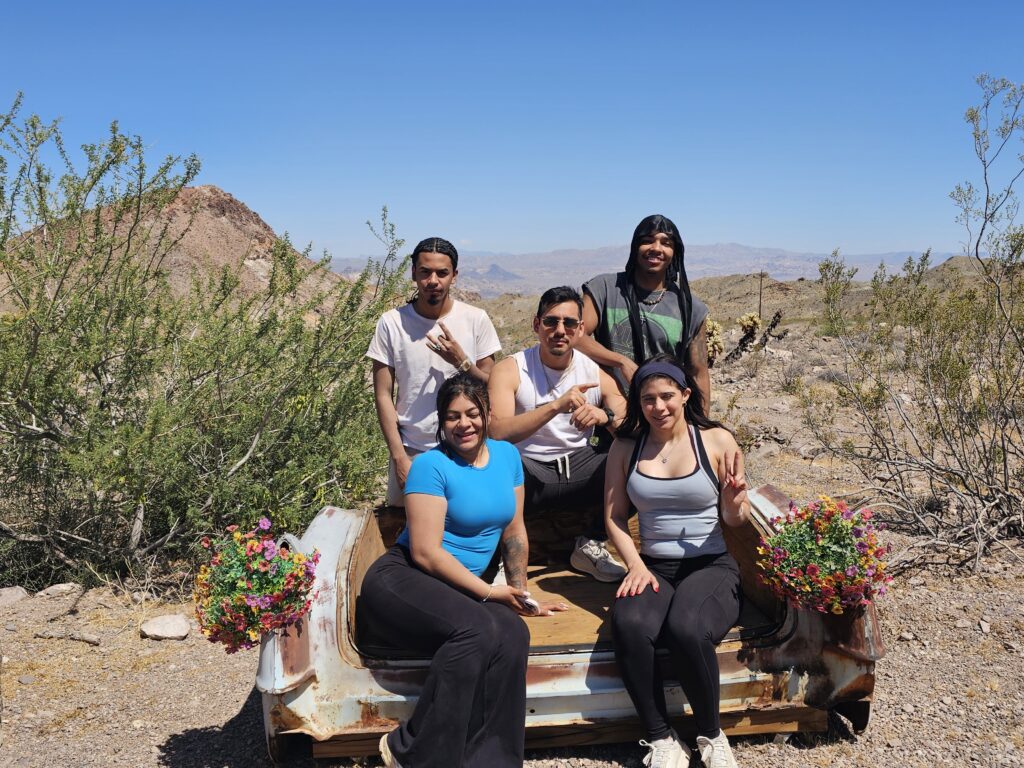 Group smiles by a car bench with flowerpots in Nevada desert near Las Vegas, perfect for Ghost Town sightseeing tours.