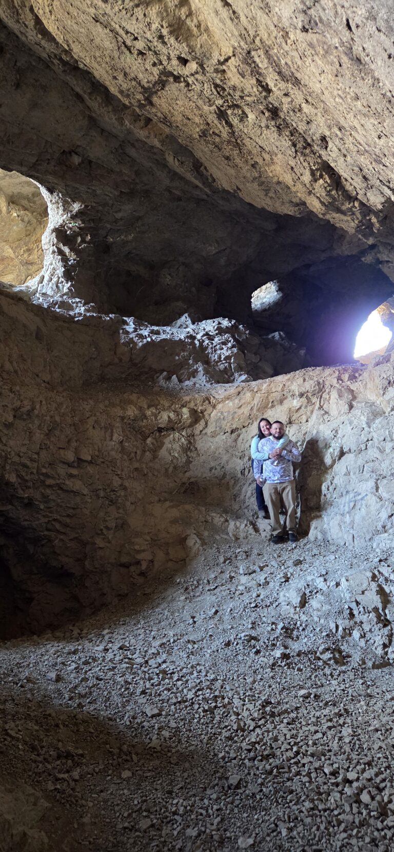 Two people stand on a rocky slope in a Nevada cave near the Colorado River, sunlight streaming in—perfect for ATV and RZR tours.
