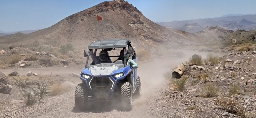 Nevada RZR off-road vehicle kicking up dust on a desert trail near Las Vegas, with riders and scenic hills under a clear sky.