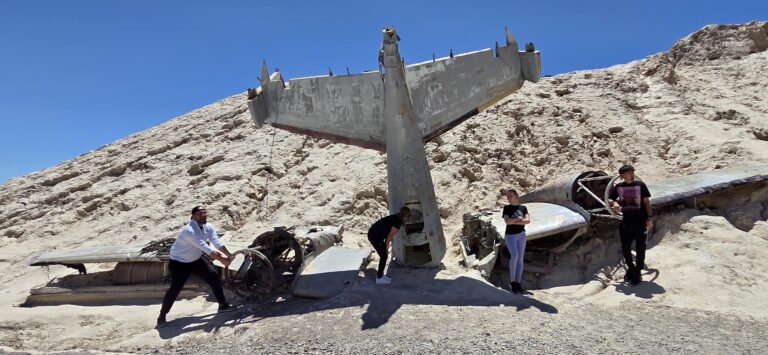 Four people pose by a crashed airplane in Nevada’s desert near Las Vegas, popular for ATV tours and ghost town sightseeing.