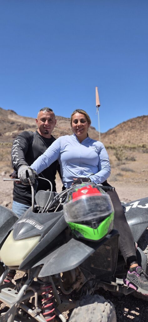 A man and woman on an ATV in Nevada desert near Las Vegas, rocky hills behind—perfect for off-road RZR tours or Ghost Town rides.