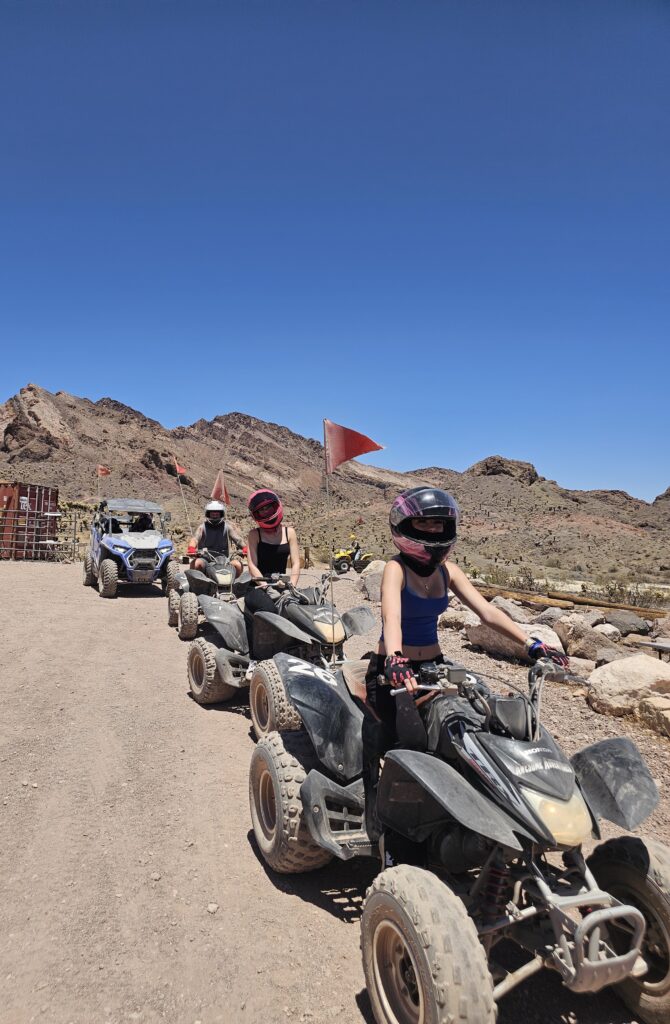ATV riders on a Nevada desert trail near Las Vegas with rocky hills, joined by a fourth RZR on an exciting ATV tour.