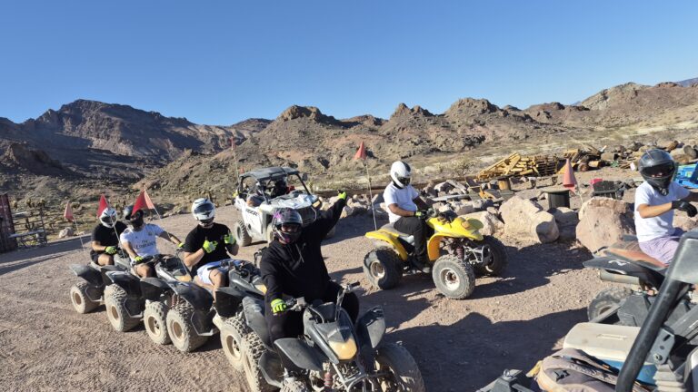 Helmeted riders on ATVs and a utility vehicle explore a rocky Nevada desert trail near Las Vegas with mountain views.