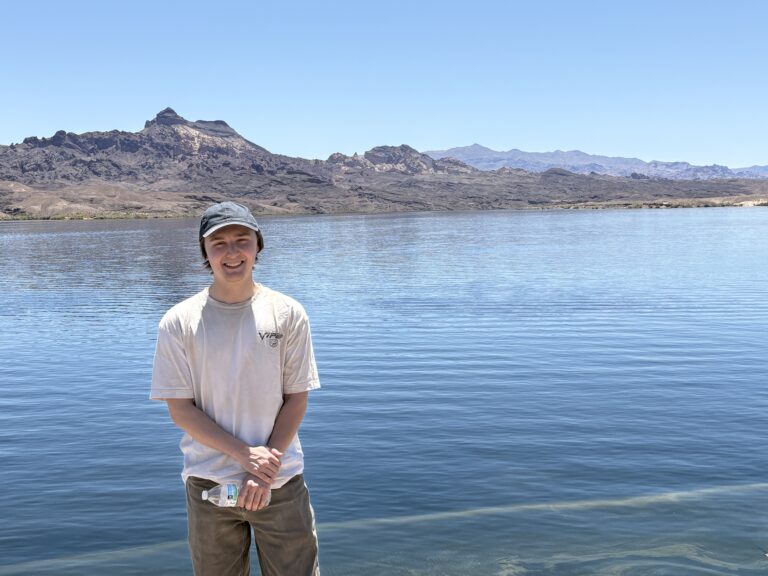 Smiling young person by the blue Colorado River near Las Vegas, Nevada, with rocky mountains and clear sky—perfect for ATV tours.