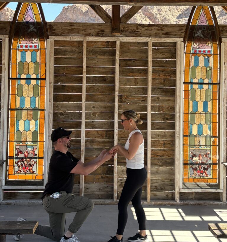 A man proposes to a woman in a rustic Nevada venue with stained glass, mountains, and Colorado River views—perfect for Las Vegas weddings.
