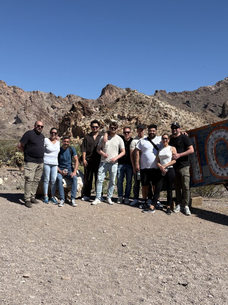 Ten friends smile together in Nevada's sunny desert, with Las Vegas mountains—perfect for ATV tours and RZR off-road rides.
