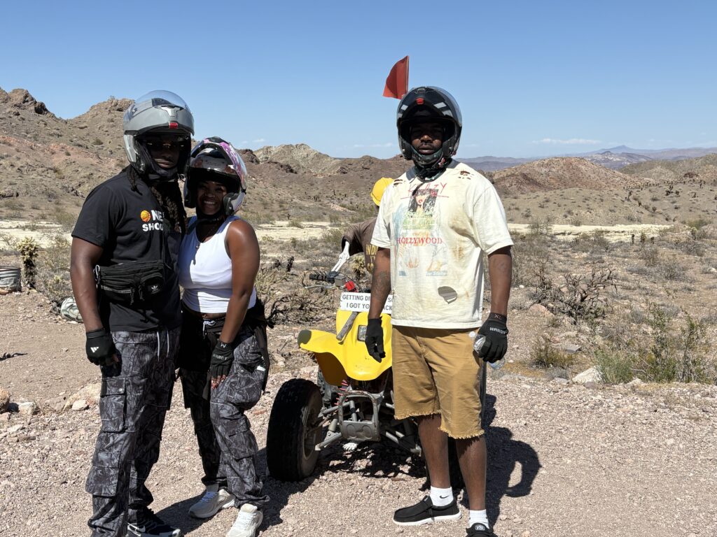 Adventurers in helmets by a yellow ATV enjoy a Nevada desert tour near Las Vegas under clear skies.