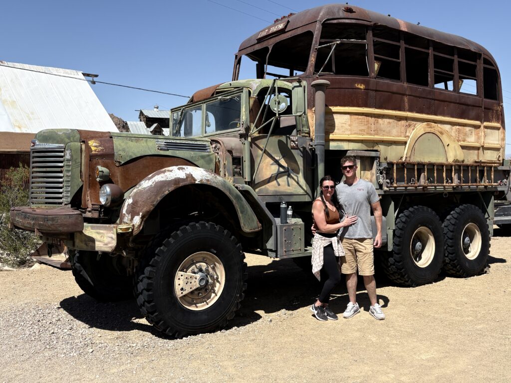 Smiling couple by a rusty custom truck-bus in Nevada, perfect for Ghost Town sightseeing or Colorado River ATV tours.