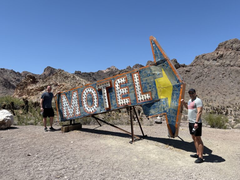 Two people by a vintage MOTEL sign in Nevada’s rocky desert, near Las Vegas, perfect for Ghost Town sightseeing adventures.