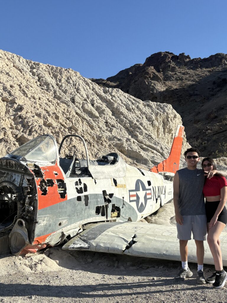 Smiling couple poses by abandoned Navy plane wreck in Nevada desert near Las Vegas, perfect for ATV tours and Ghost Town sightseeing.