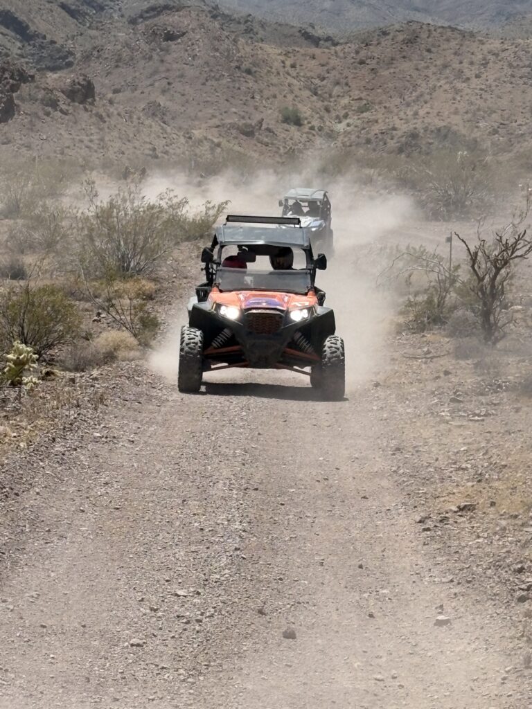 ATV tour in Nevada: red off-road vehicles speed along a dusty desert trail near Las Vegas, rocky hills in the background.