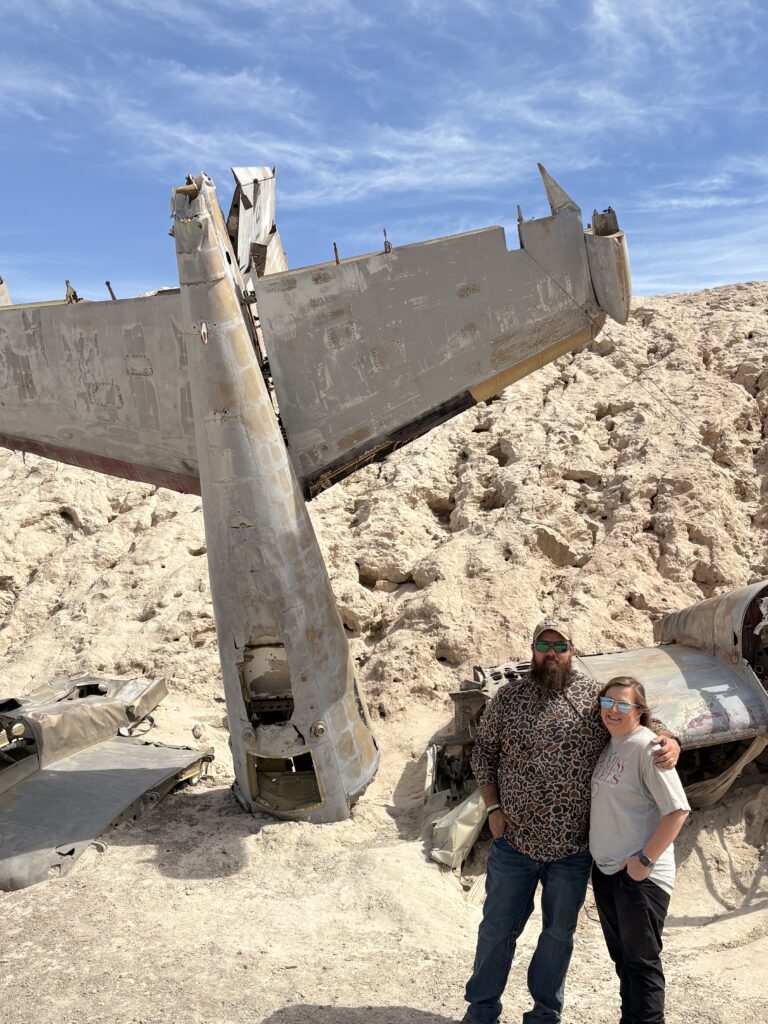 Smiling duo by airplane wreck in Nevada desert near Las Vegas, perfect for ATV tours and Ghost Town sightseeing adventures.