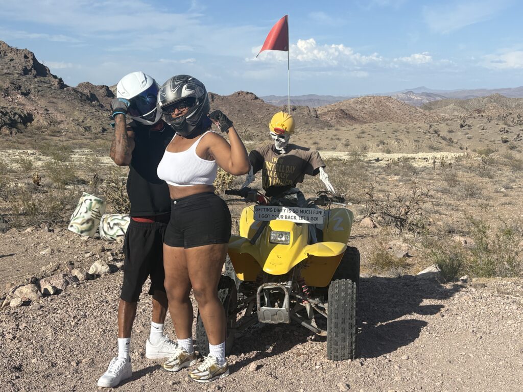 Helmeted riders pose by a yellow ATV in Nevada’s rocky desert near Las Vegas on an ATV tour, mountains behind.
