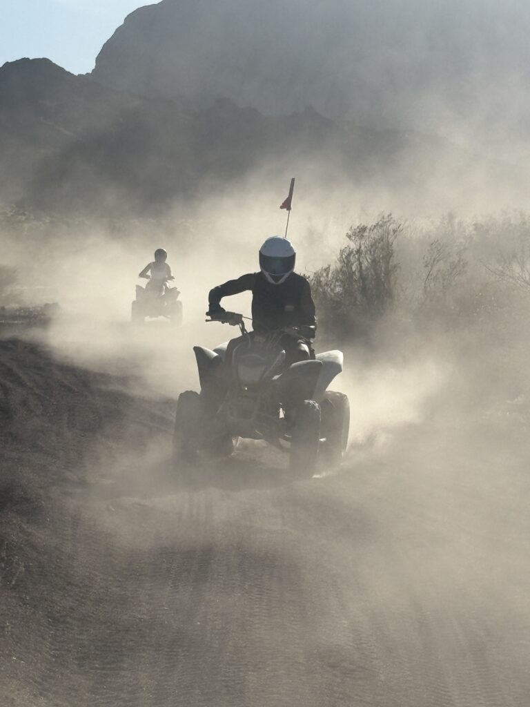 Adventurers on an ATV tour ride dusty trails near Las Vegas, Nevada, with mountains and sunlight in the background.