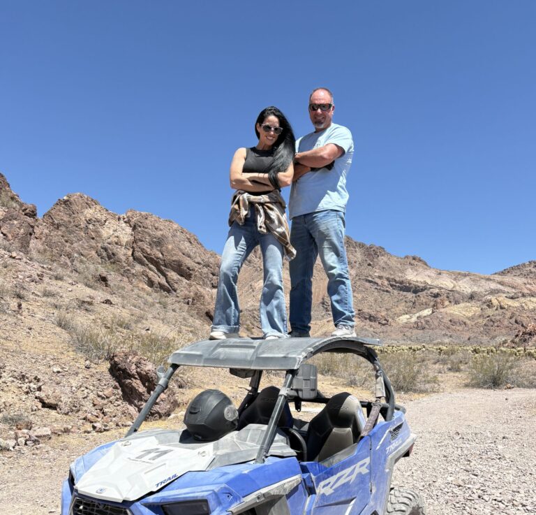 Adventurers atop a blue off-road vehicle in Nevada, near Las Vegas mountains, ready for RZR ATV tour under the clear sky.