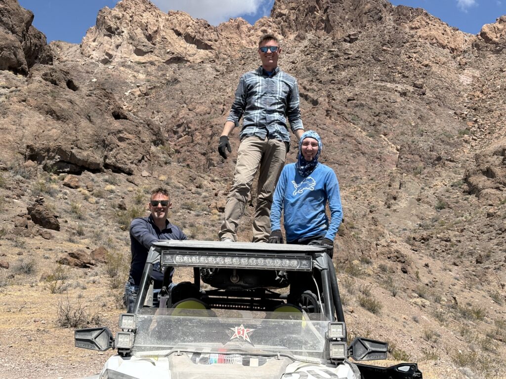 Three men with an off-road RZR in Nevada desert near Las Vegas, brown mountains behind—perfect for ATV tours and Colorado River views.