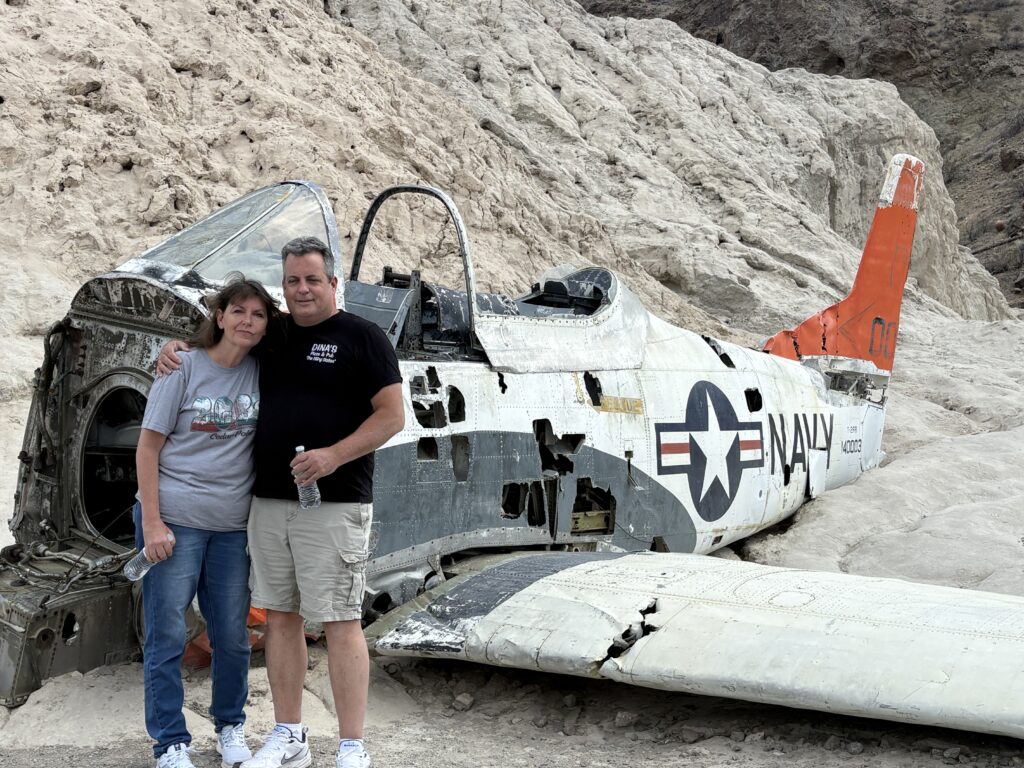 Couple poses arm in arm by abandoned Navy aircraft wreck in Nevada desert near Las Vegas, perfect for ghost town sightseeing.