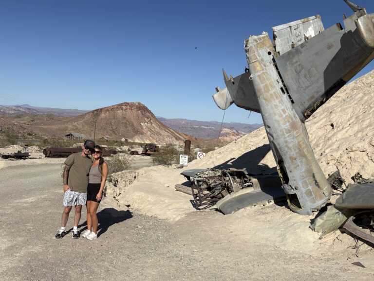 Couple near rusted crashed airplane on Nevada desert road, rocky hills; perfect for ATV tours or Ghost Town sightseeing near Las Vegas.