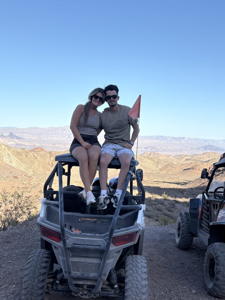 Happy couple atop an ATV with red flag, enjoying Nevada desert views near Las Vegas and Colorado River during off-road RZR tour.