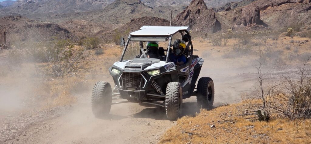 Helmeted riders drive a side-by-side ATV on a dusty Nevada desert trail near Las Vegas during an exciting RZR off-road tour.