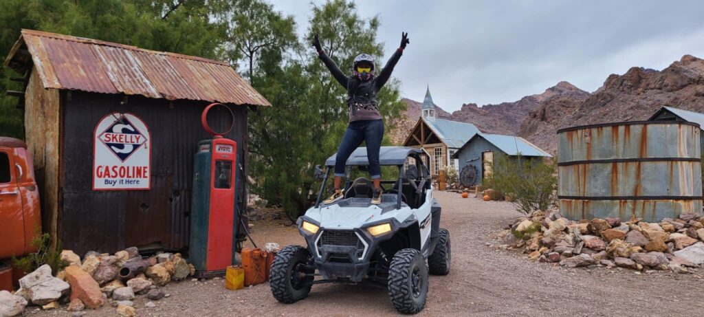 Rider in helmet celebrates atop ATV in Nevada ghost town near Las Vegas, vintage buildings behind—perfect for ATV tours or RZR rides.