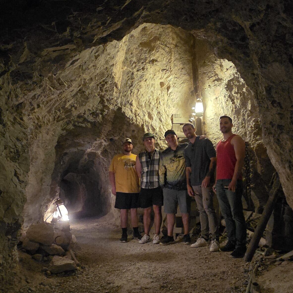 Five visitors explore Techatticup gold mine near Las Vegas, Nevada, lantern-lit tour, rocky walls, and authentic ghost town vibe.