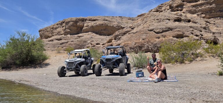 Couple relaxing by the Colorado River near Las Vegas, with ATVs on rocky Nevada shore and scenic desert formations in the background.