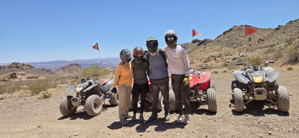 Adventurers in helmets pose by quad bikes in Nevada desert near Las Vegas, ready for an ATV tour under clear blue skies.