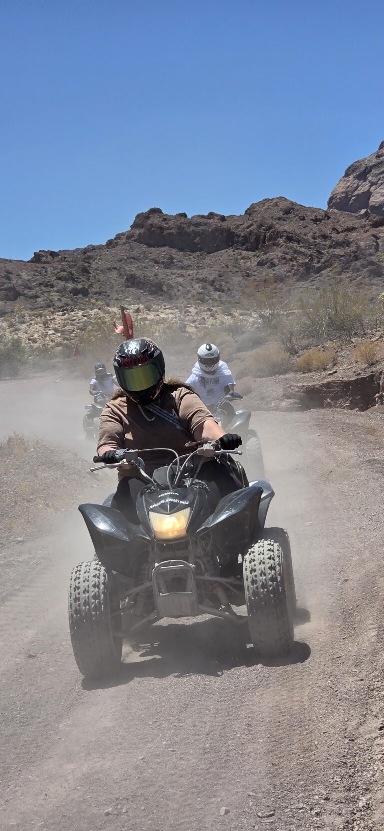 ATV riders explore a dusty Nevada desert trail near Las Vegas under blue skies, helmeted and ready for thrilling RZR off-road tours.