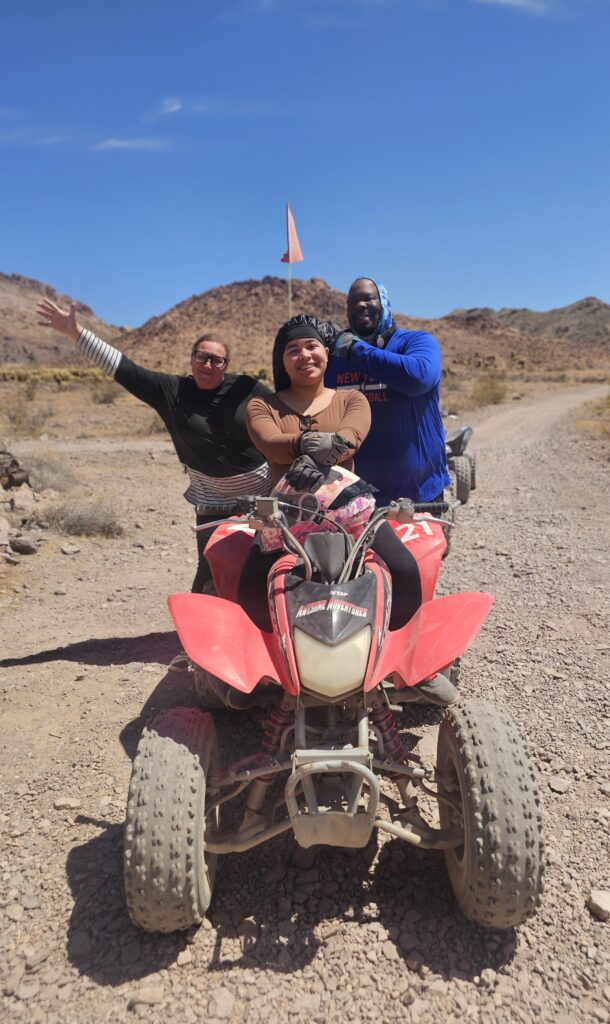Smiling group posing on a desert ATV tour in Nevada near Las Vegas, with red ATV and clear blue sky.