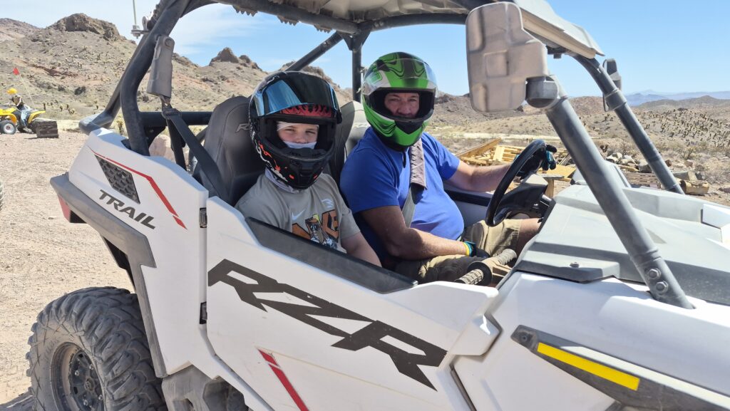 Two riders in helmets enjoy a white RZR on a Nevada desert trail near Las Vegas, perfect for RZR off-road and ATV tours.