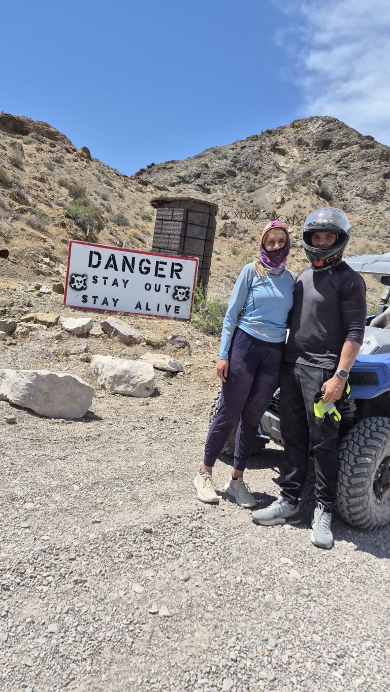 Adventurers in helmets stand by an ATV near Las Vegas, Nevada, beside a DANGER STAY OUT sign on a rocky desert RZR tour.