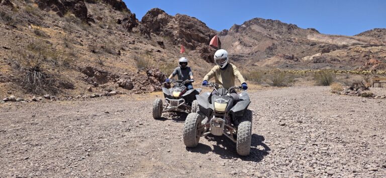 ATV tour riders in helmets explore a rocky desert trail near Las Vegas, Nevada, with mountains and sparse vegetation.