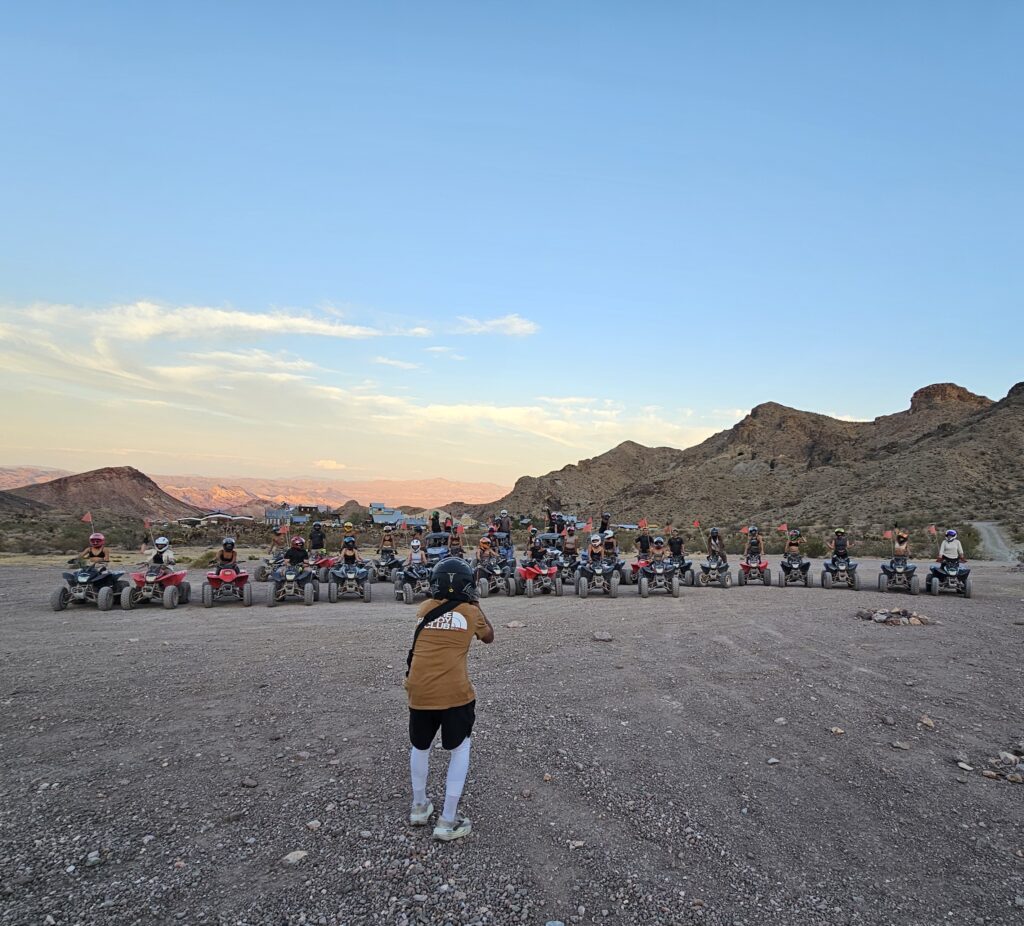 Person overlooks a group on ATVs lined up for a Nevada desert RZR tour near Las Vegas at sunset, rocky hills in the background.