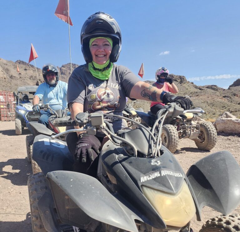 Group on an ATV tour near Las Vegas rides dirt trails in Nevada’s rocky desert, red flags flying, mountains in the background.