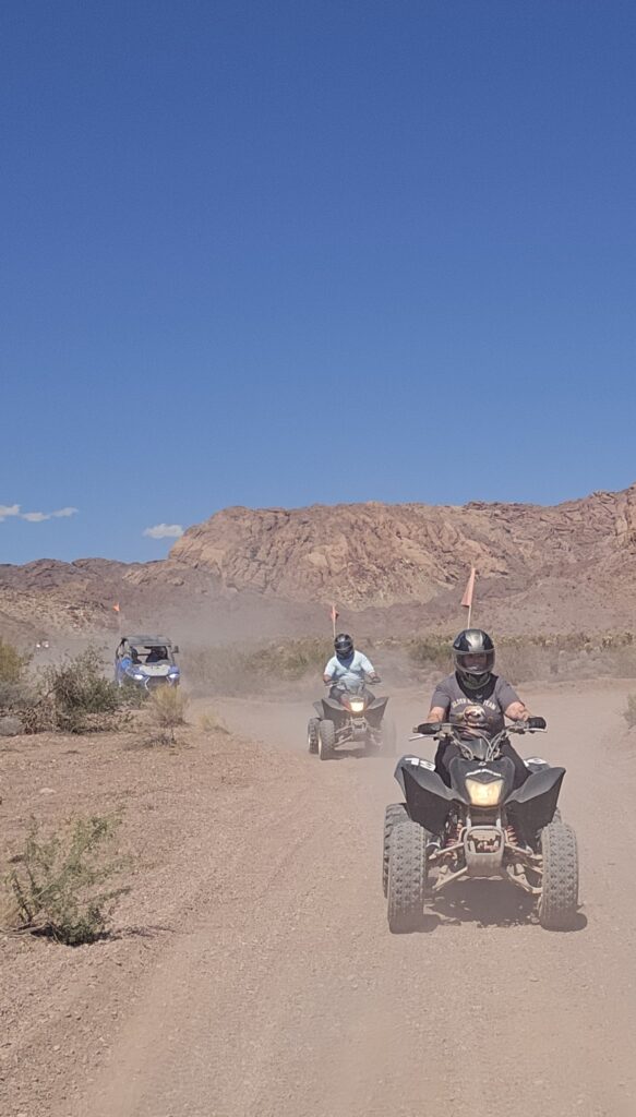 ATV and dune buggy riders explore a dusty Nevada desert trail near Las Vegas with rocky hills under clear blue skies.