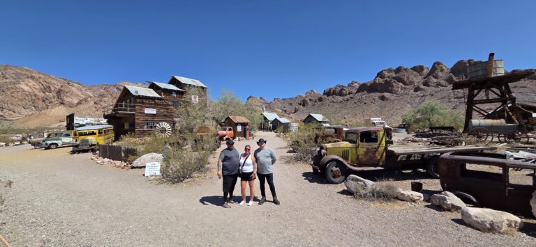 Visitors stand by historic wooden buildings and rusty cars in a Nevada ghost town near the Colorado River on a Las Vegas ATV tour.