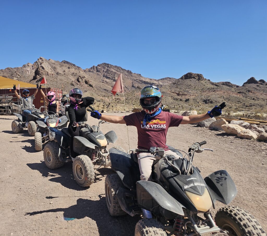 Group on ATVs with helmets enjoys Nevada desert near Las Vegas, stretching arms wide during epic ATV tour with mountain views.