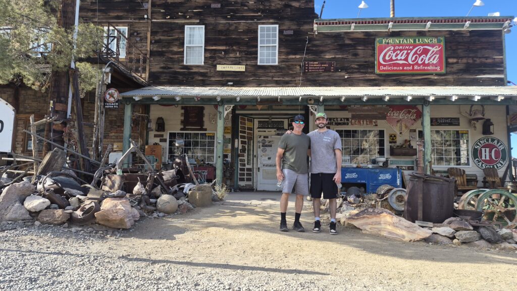 Smiling friends outside a rustic Nevada ghost town near the Colorado River, vintage signs and mining gear, perfect for ATV tours.