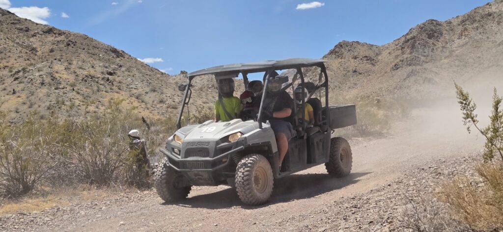 ATV tour near Las Vegas: Four ride a rugged off-road vehicle on a dusty Nevada trail beneath blue skies and rocky desert views.