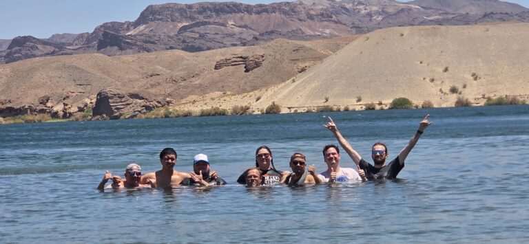 Group enjoying the Colorado River near Las Vegas, smiling in the lake with Nevada mountains and arid hills under clear skies.