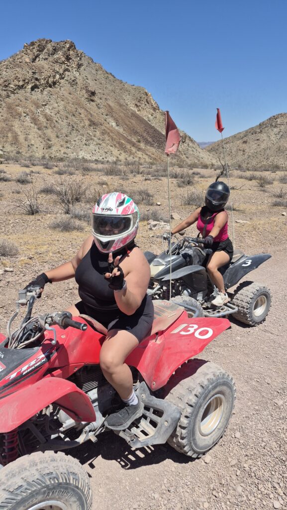 Riders in helmets enjoy a Nevada ATV tour near Las Vegas, cruising red ATVs on desert trails with mountains and dry bushes.
