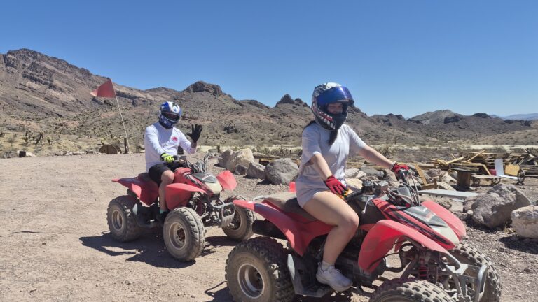 Two riders on red ATVs explore a rocky Nevada trail near Las Vegas, with mountains under blue sky—perfect for ATV tours.